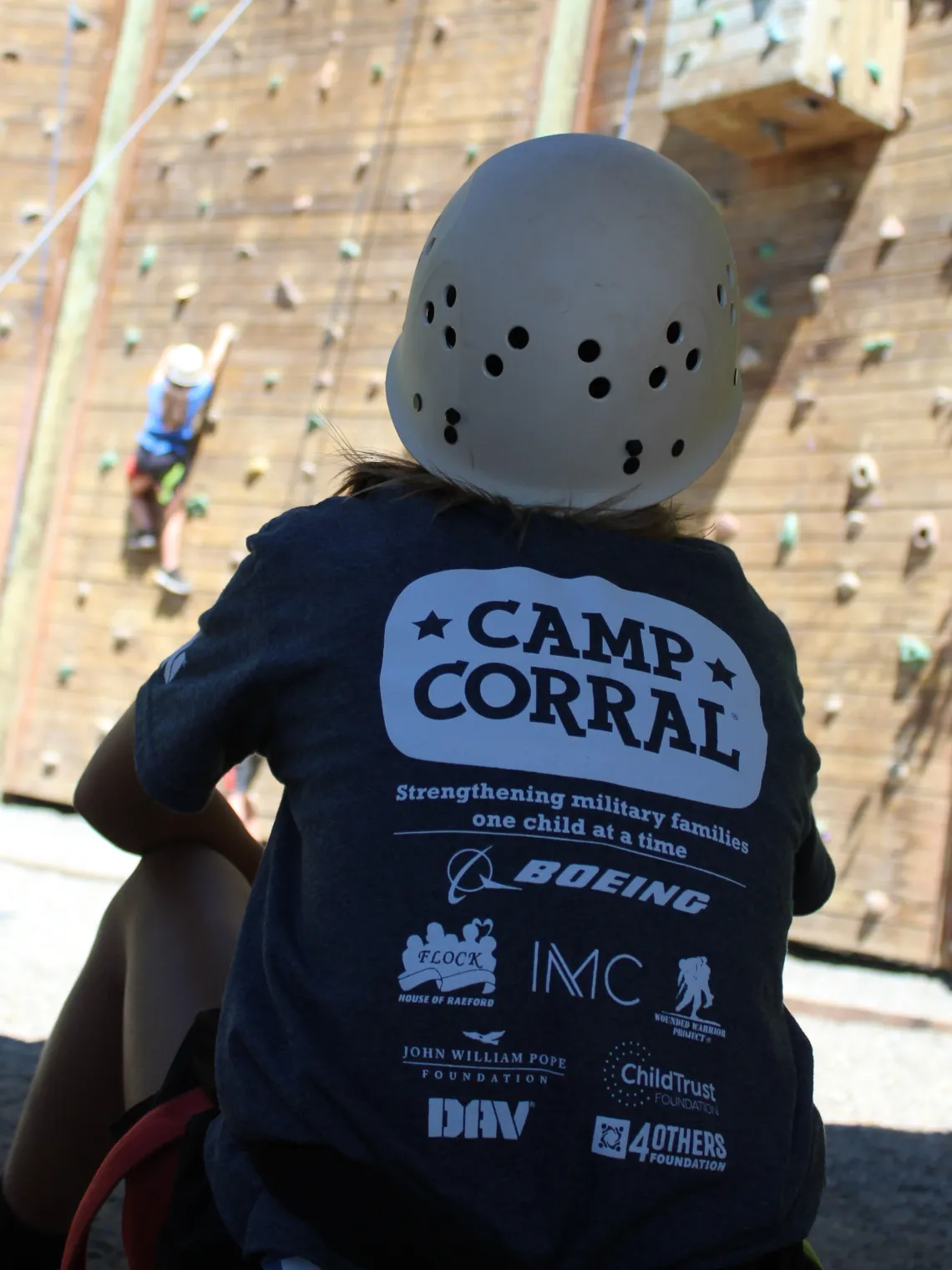 Person sitting on the ground looking up at a climbing wall