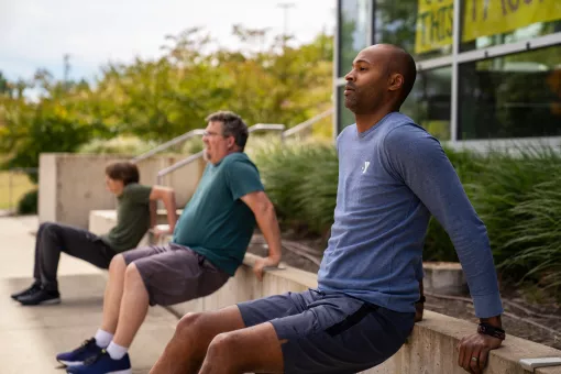 An African American man in a blue Y shirt leads two men in an outdoor boot camp.