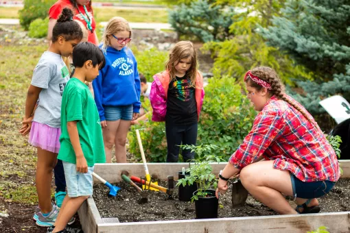Children and an instructor gather around a planter box.