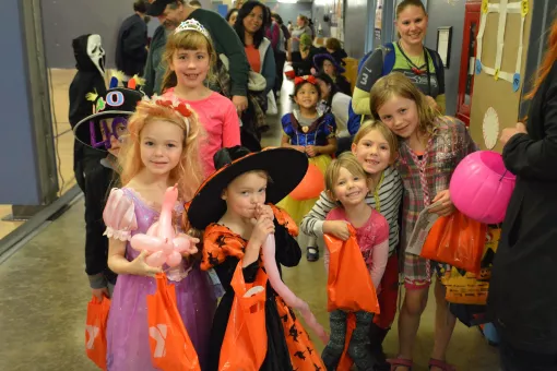 Groups of children trick-or-treat at the YMCA as witches, princesses, ghosts and more. They are smiling and holding bags of candy!