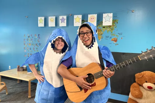 Instructors Lauren and Gabriel are in shark costumes and smiling as Gabriel holds an acoustic guitar.