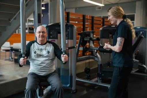 Wellness Coach Becca provides guidance to a member using an upper body piece of equipment.