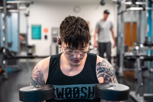 A young Asian American man reflects and holds two 45 pound free weights at the University YMCA Student Center.