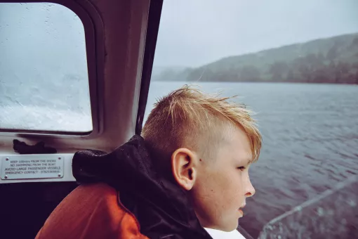 A young boy looks out over the water on a gray day. His eyes are off camera centered on what's beyond the frame.