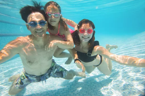 An Asian American man swims underwater with two daughters in a Y pool.