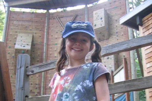 Photo of camper posing in front of the climbing wall at YMCA Camp Seymour