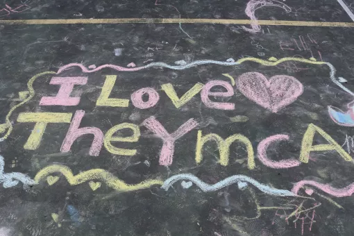 Sidewalk chalk art from a YMCA camper reading "I love the YMCA"