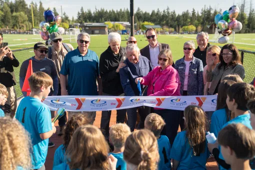 Ribbon‑cutting ceremony at the Gig Harbor YMCA sports field with community members and youth.