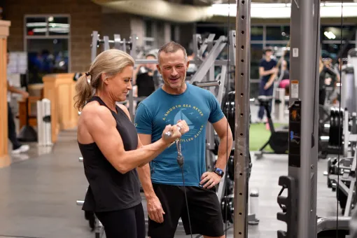 Two adults exercise at a cable machine in a gym.