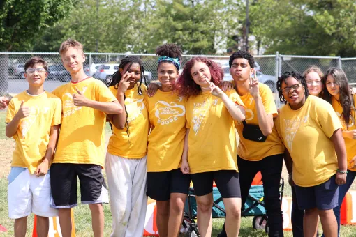 Group of YMCA summer camp participants in matching yellow camp shirts standing together outdoors on a grassy field during a summer camp activity at the YMCA of Pierce and Kitsap Counties.