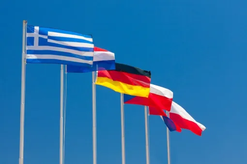 International flags representing multiple countries wave against a blue sky, symbolizing cultural exchange, global diversity, and international staff at YMCA Camp Seymour.