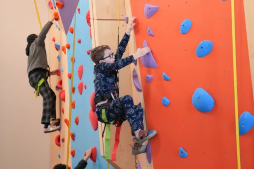 Child climbing the Liz Rocks Climbing Wall at the YMCA, building strength, confidence, and coordination through active youth recreation.