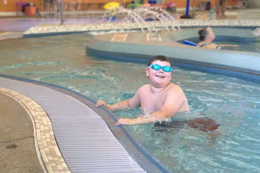 Beary wears swim goggles while holding onto the edge of the lazy river at the Gordon Family YMCA aquatic center during a YMCA swim lesson.