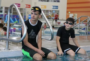 Swimming lesson participants sitting on the pool's edge while receiving instruction at the YMCA
