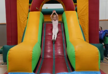 Action shot of a Healthy Kids Day participant going down the bounce house slide at the Mel Korum Family YMCA