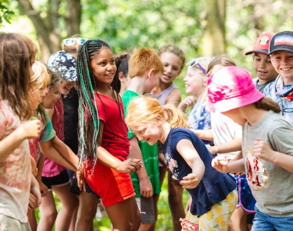 A group of kids dressed in different shades of t-shirts and shorts are laughing, smiling, and having fun. 