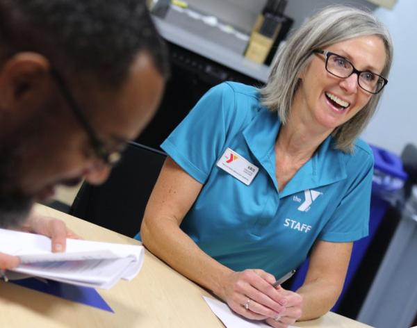 A smiling member of the YMCA team smiles another another team member beyond the photographer.