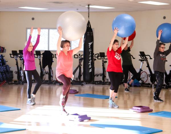 A group of active older adults holds yoga balls above their head as they work on movement and balance in a core yoga class. 