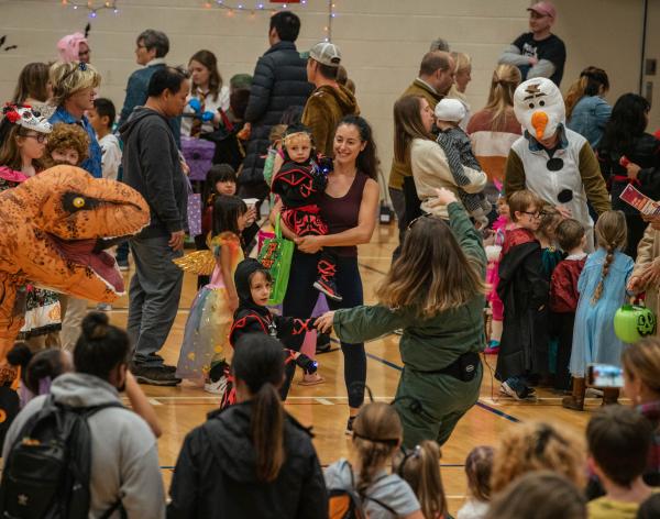 A crowd of adults and children are dressed up to celebrate the season. A raptor costume stands out in the forefront. 