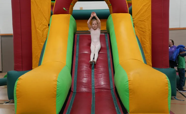Action shot of a Healthy Kids Day participant going down the bounce house slide at the Mel Korum Family YMCA