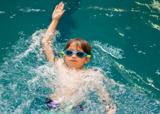A child swims in water while wearing goggles.