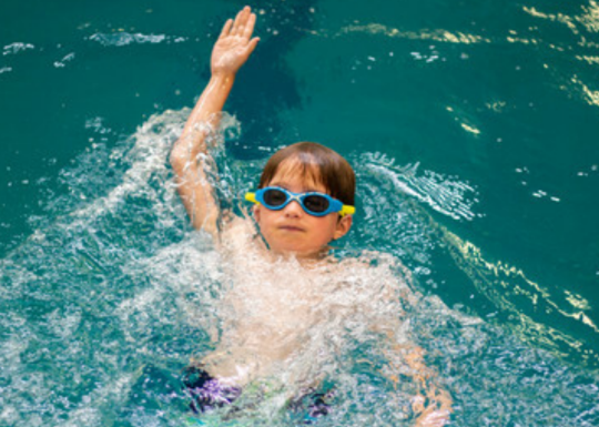 A child with goggles swimming in a YMCA pool.