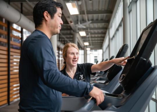 Wellness Coach Becca provides an equipment orientation on a treadmill to a member.