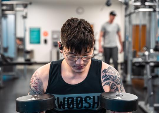 A young Asian American man reflects and holds two 45 pound free weights at the University YMCA Student Center.