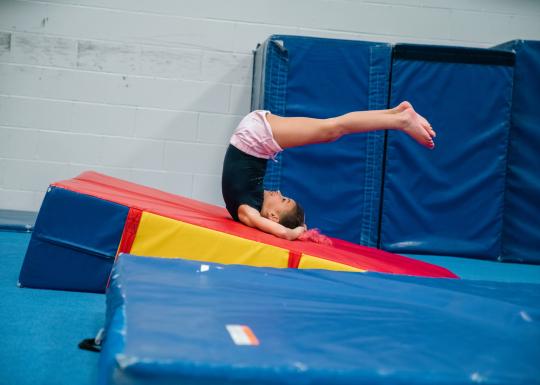 Toddler gymnast tumbles backwards on foam ramp at the YMCA