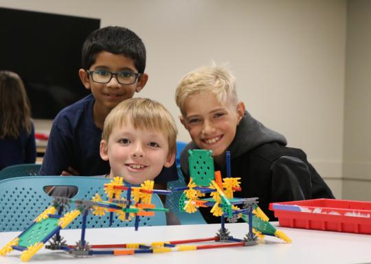 Summer camp participants pose behind a Kinex building block creation at the YMCA