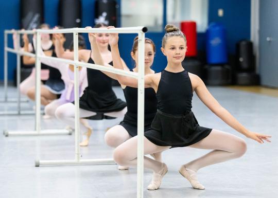 Youth ballet students practicing technique and balance exercises at a ballet barre.