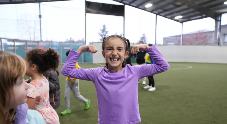 Camp participant poses by flexing during sport time in the covered playfield at the YMCA
