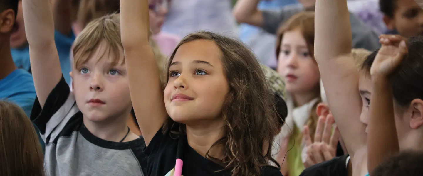 Campers raise their hands during an activity at the YMCA