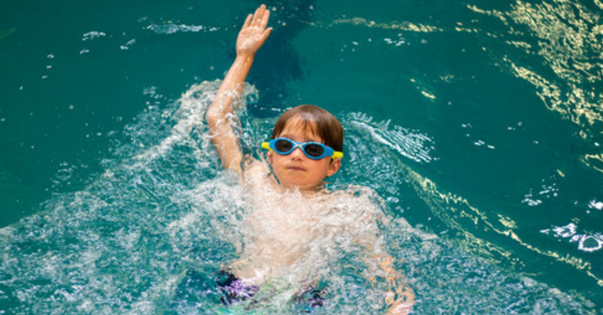 A child with goggles swimming in a YMCA pool.