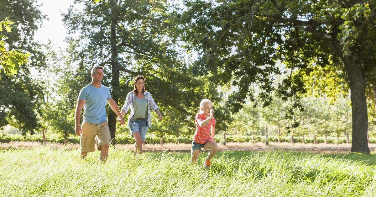 Two adults and a child walk through grass.