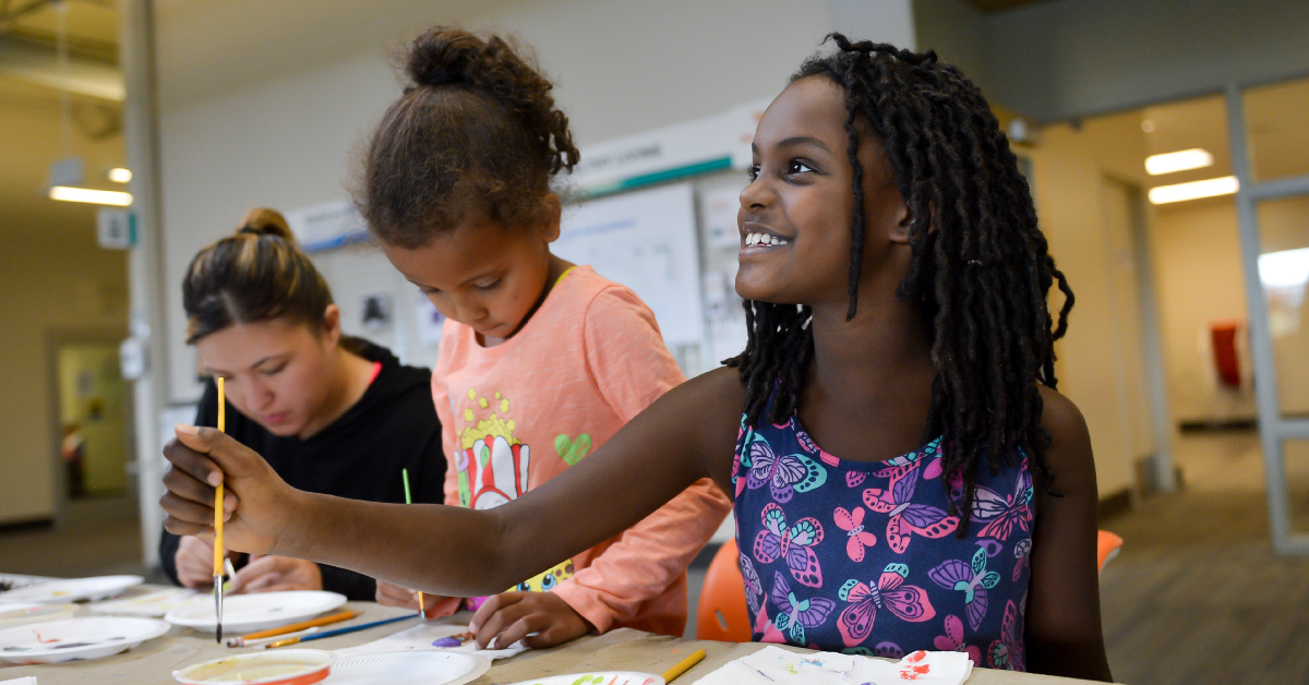 An adult and two children attend an arts class where they paint together.