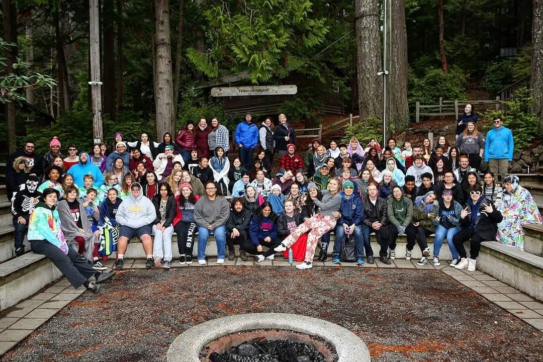 A large group of students and youth leaders surround a fire pit.