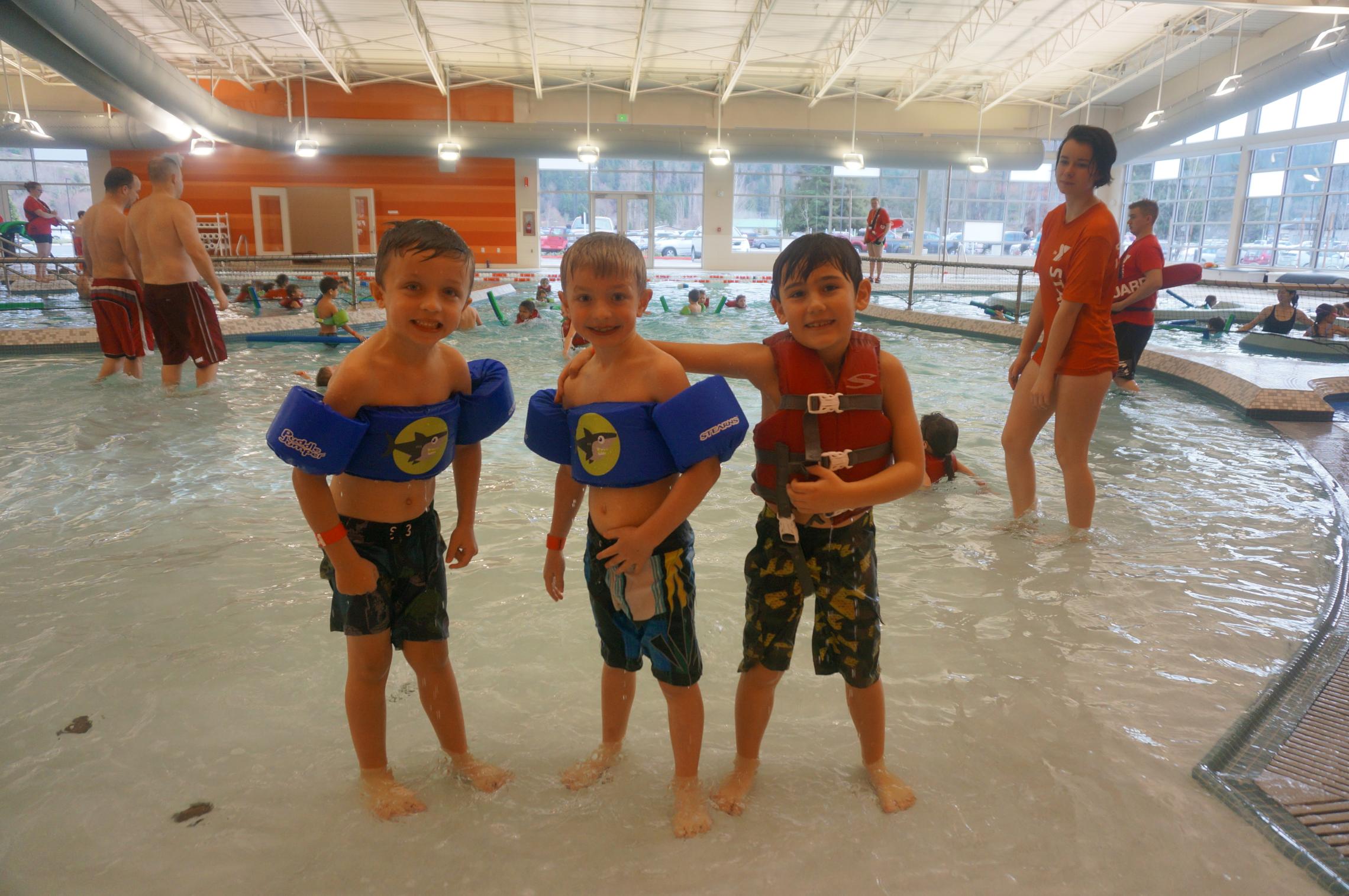 3 children smiling at the shore of the wading pool
