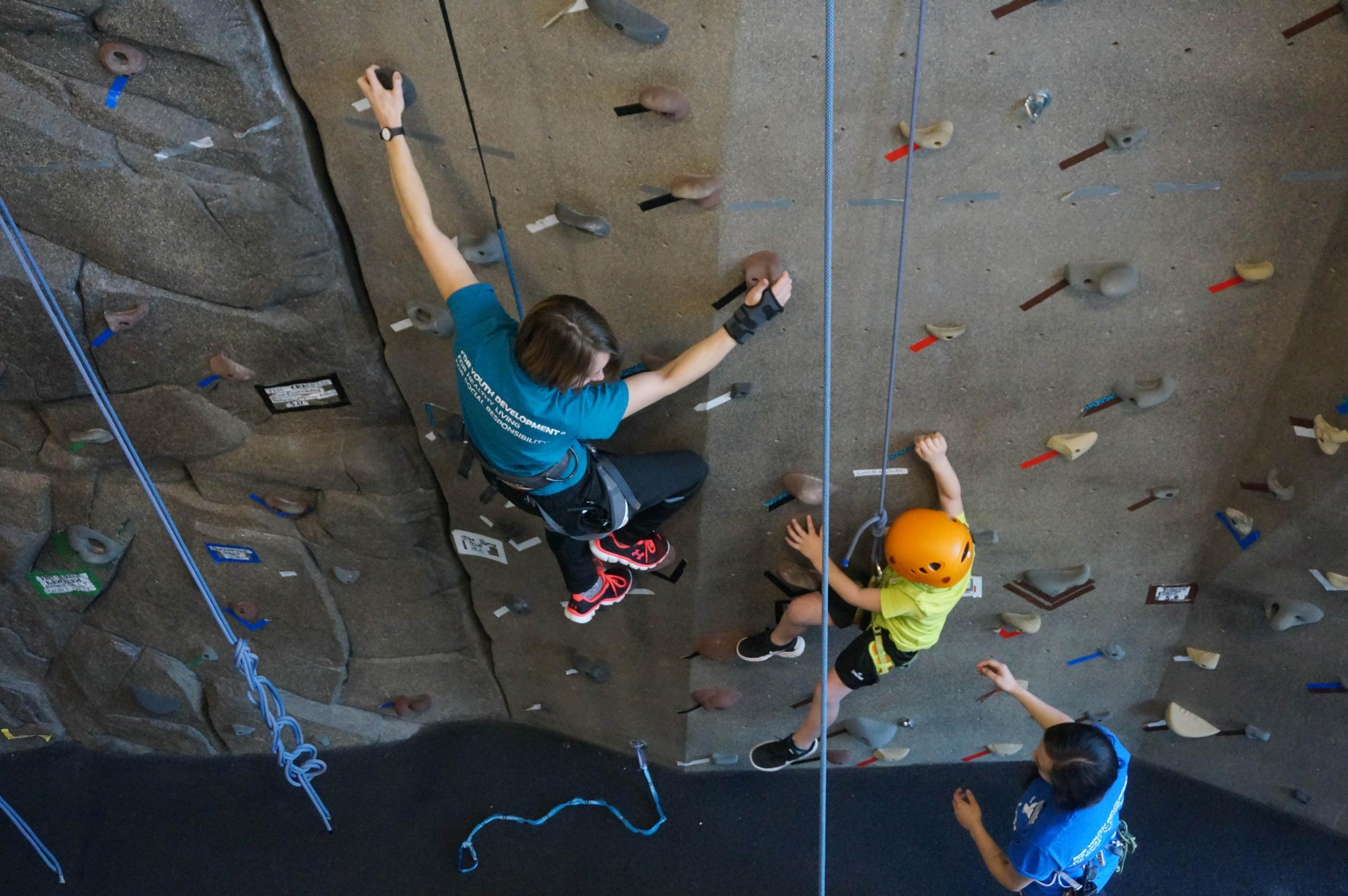 Staff leading winter break camp participant up rock climbing wall route