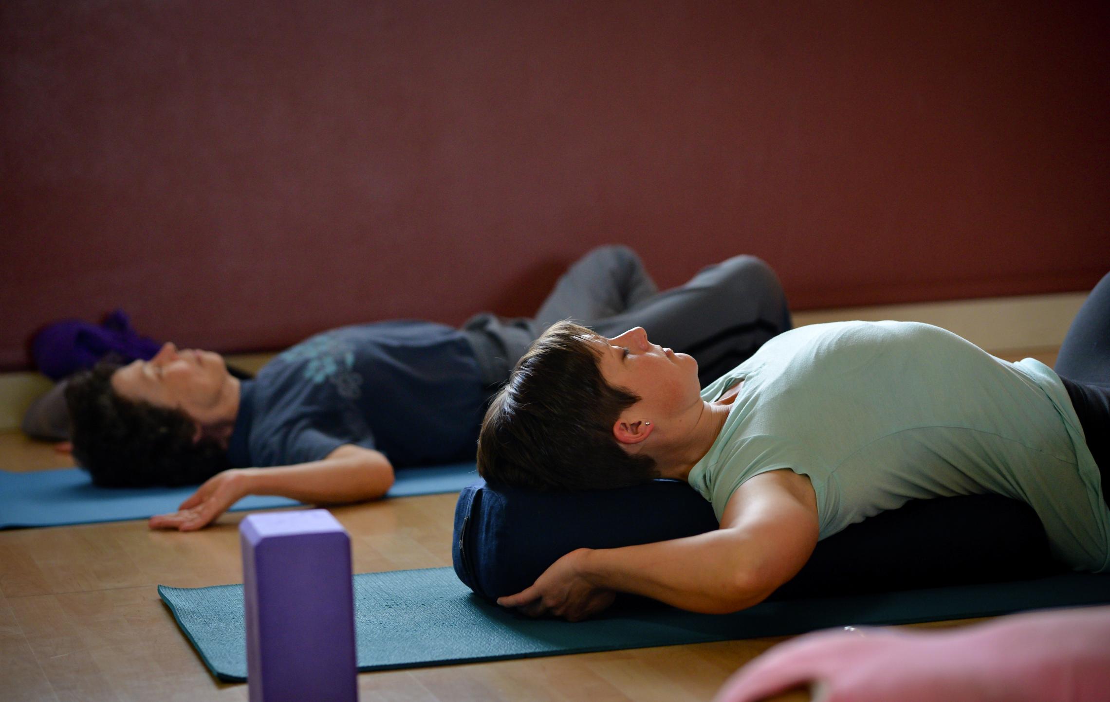 Two people practice yoga while lying on their backs at Morgan Family YMCA.