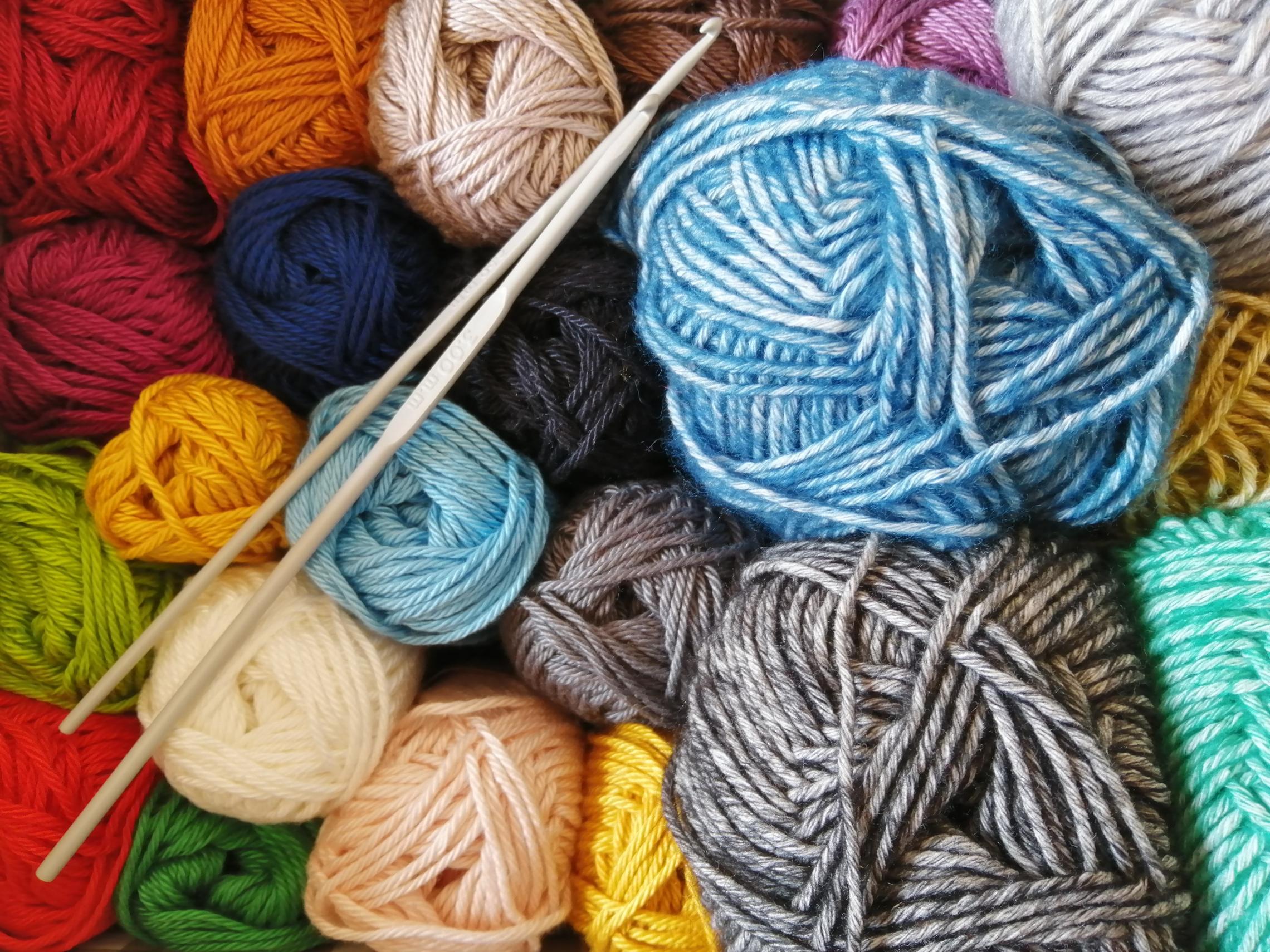 Balls of colorful yarn are viewed from above along with a set of knitting needles.