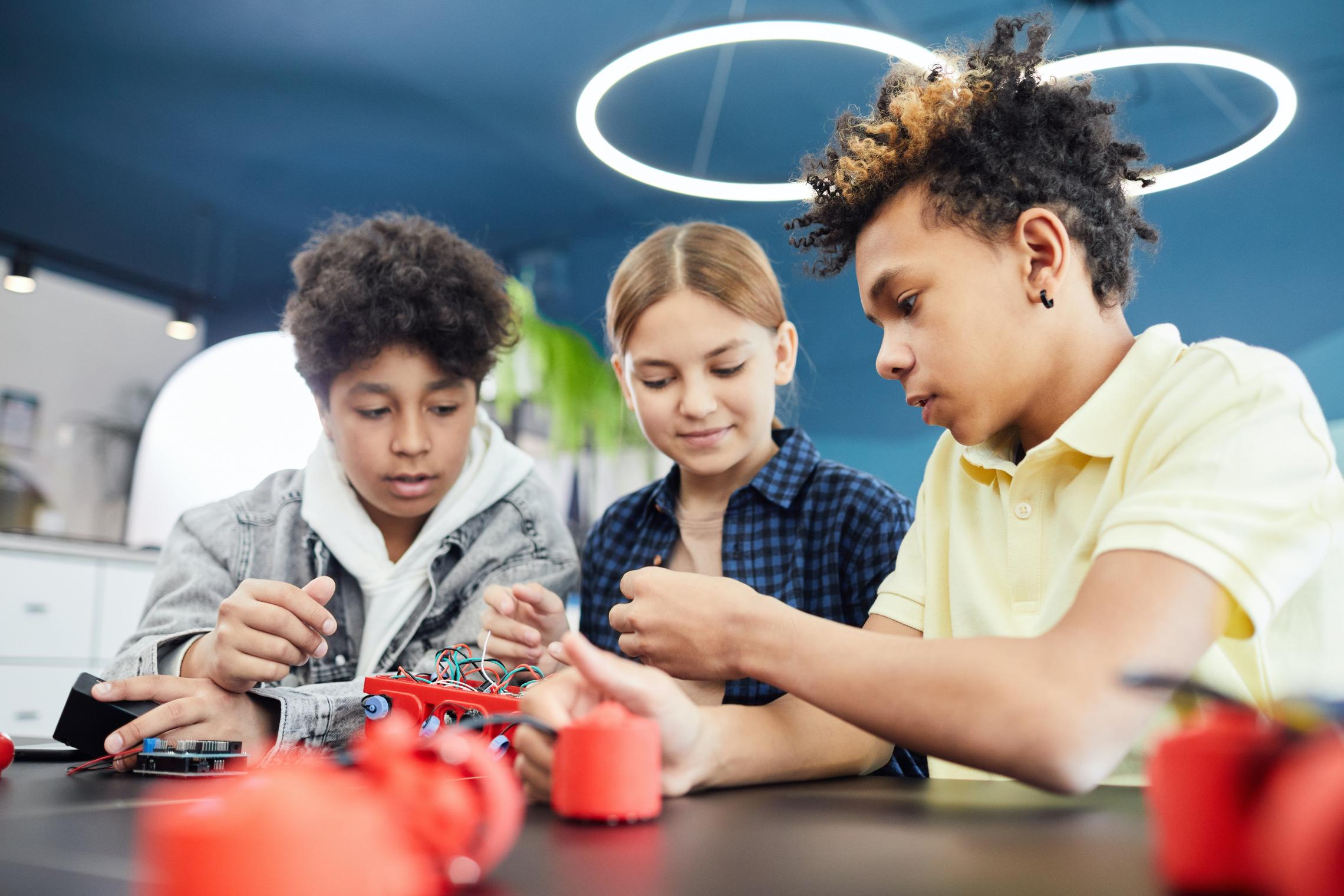 Three pre-teens collaborate together on a robotics project.