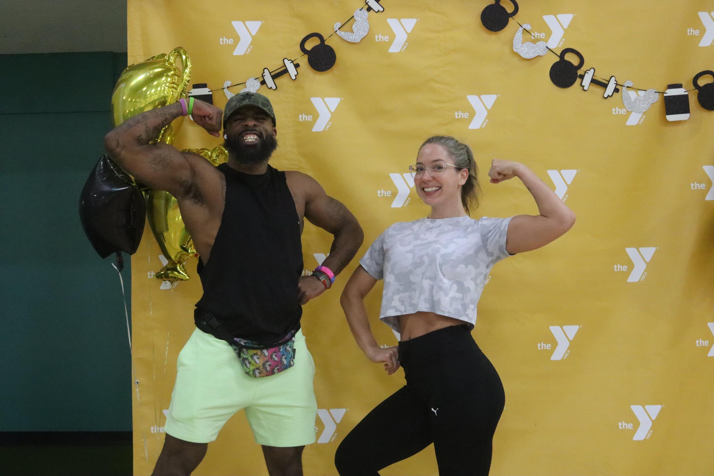 An African American man and a Caucasian woman pump their biceps in front of a yellow step and repeat with the Y logo.