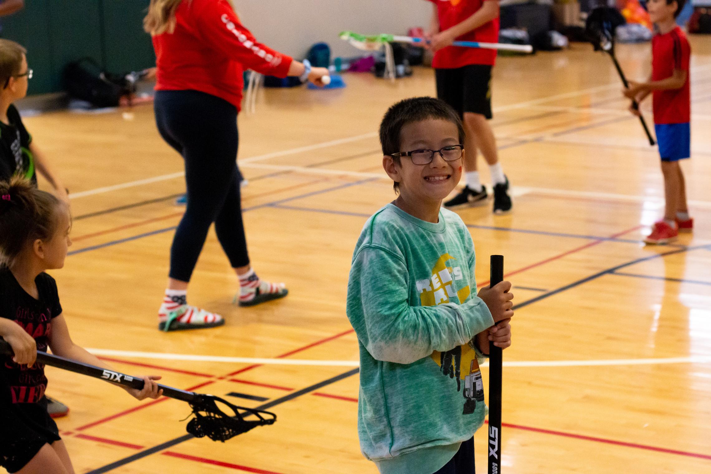 Summer camp participant posing with a lacrosse stick at the YMCA
