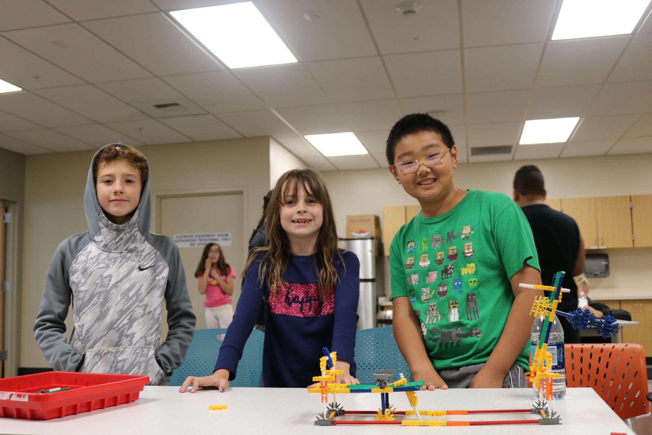 Summer day campers pose behind kinex building block structure at the YMCA