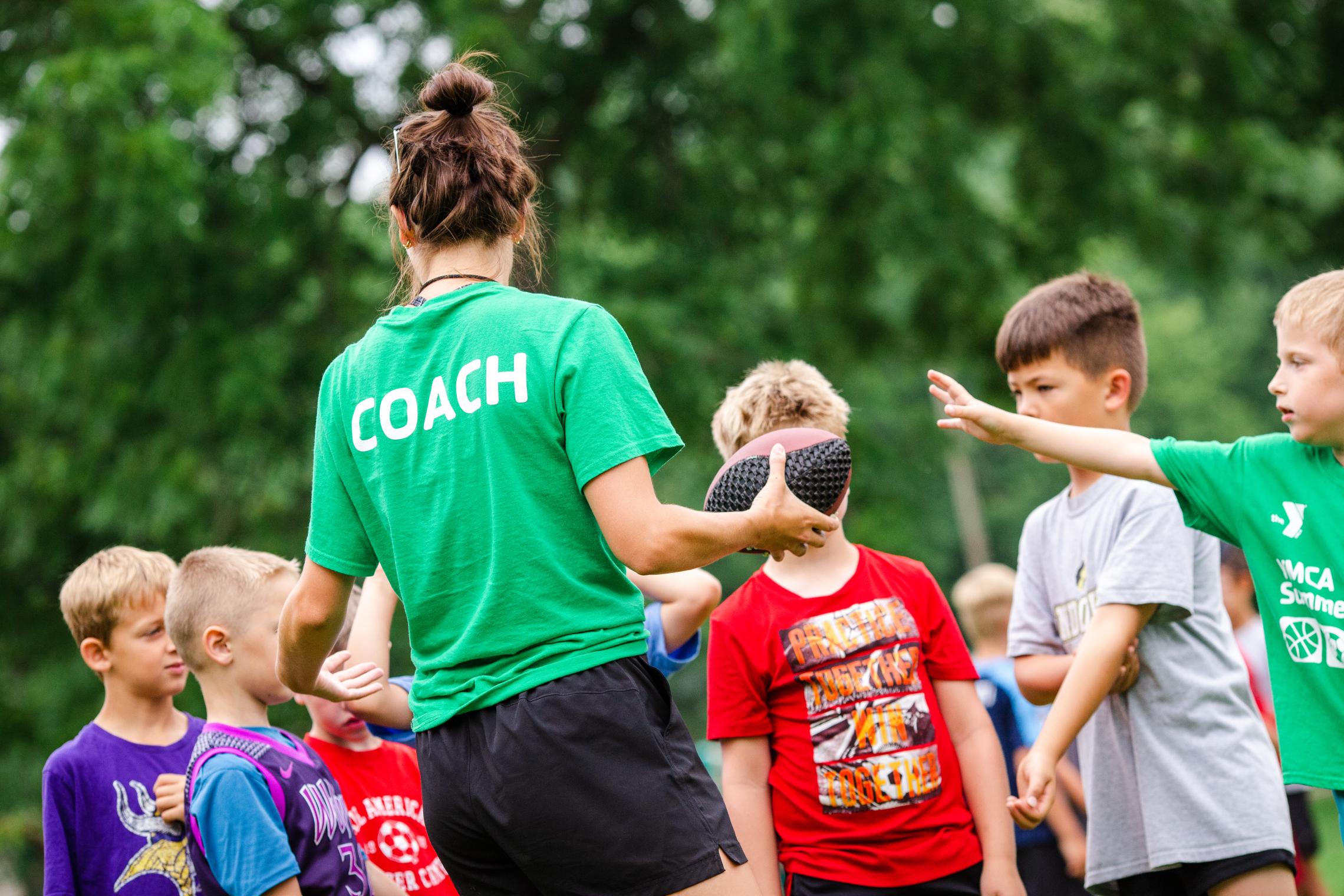 Youth football coach pulls team in for a huddle during a game at the YMCA