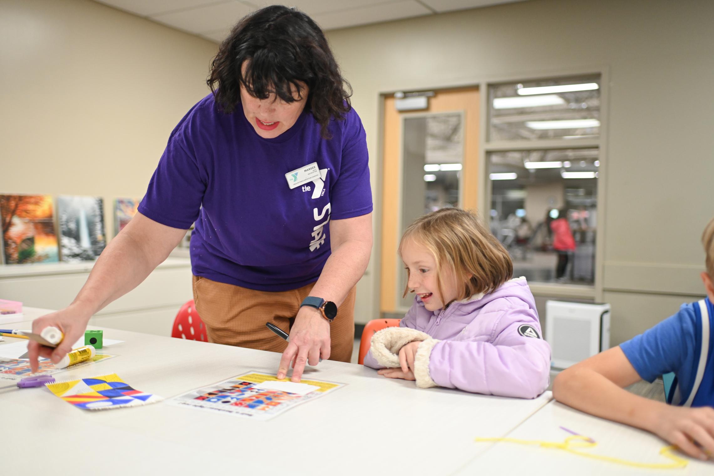 Camper and staff bond over craft time indoors during camp at the YMCA