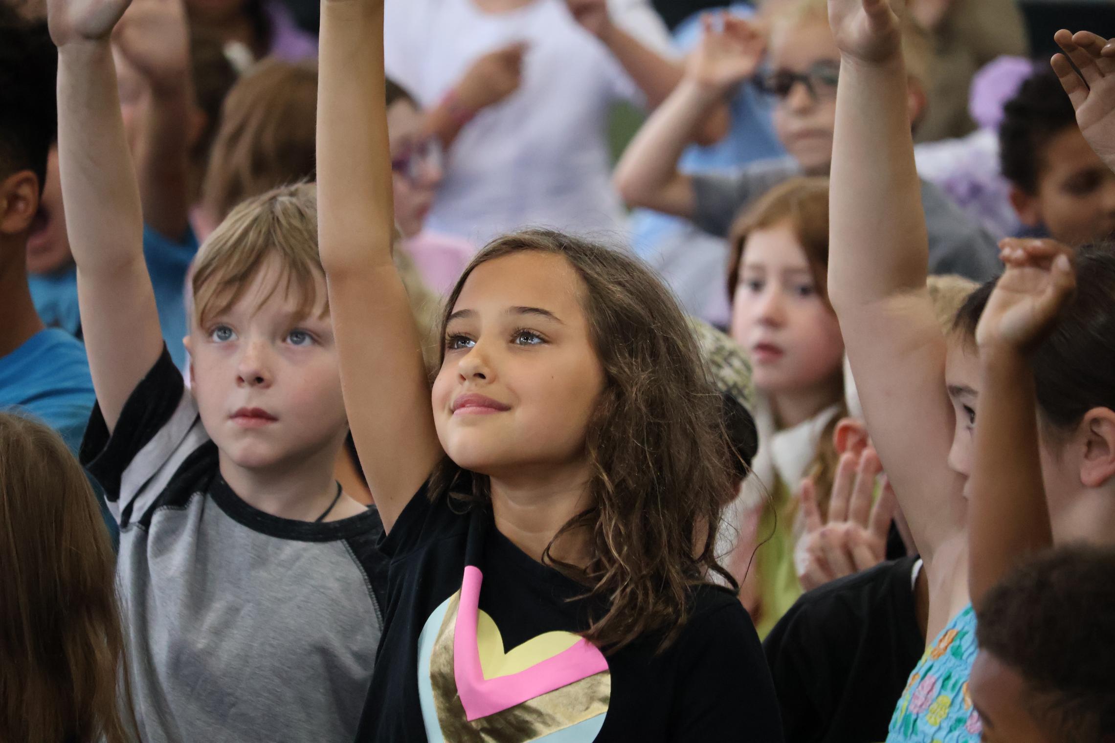 Campers raise their hands during an activity at the YMCA