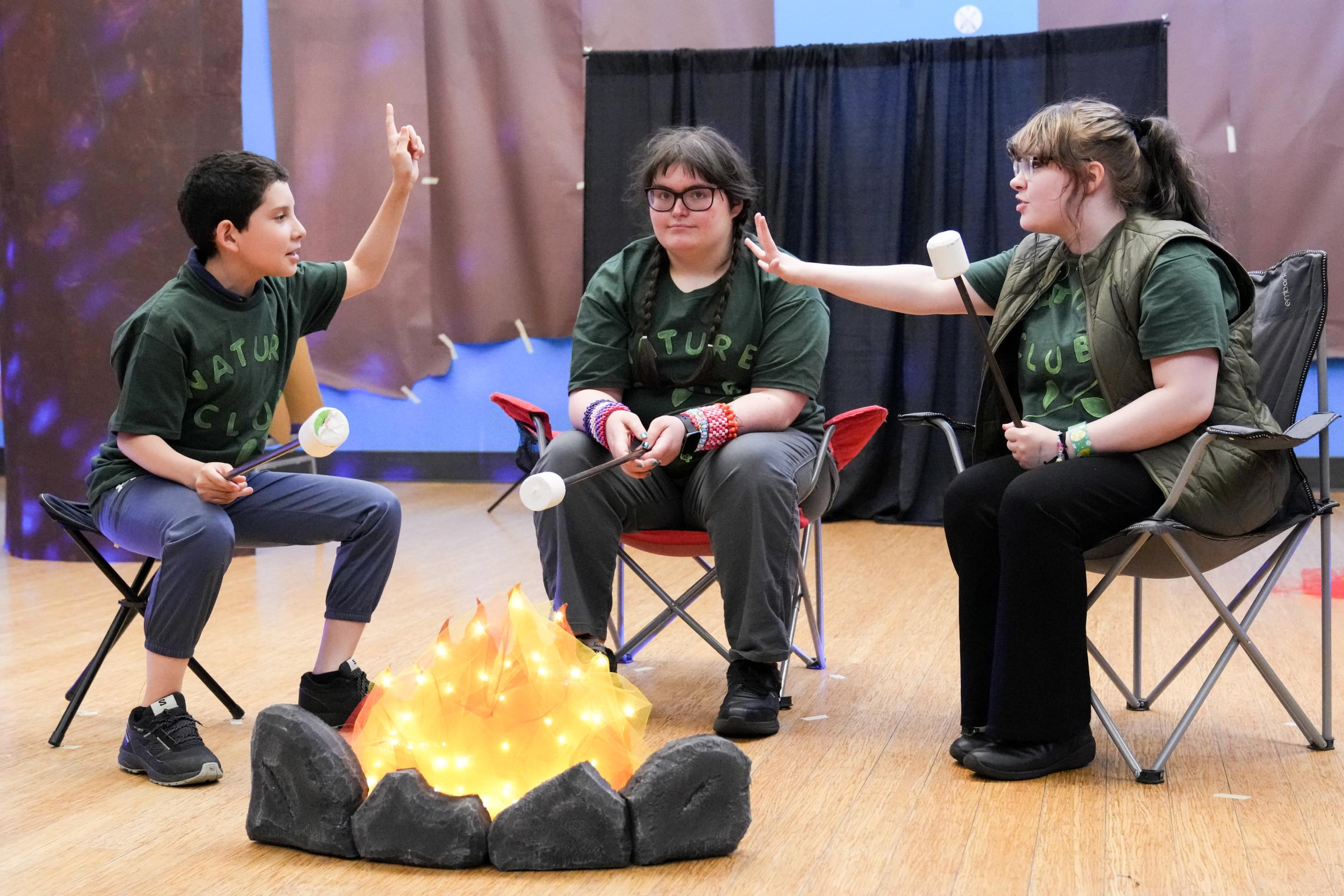 Three youth performers around a campfire prop
