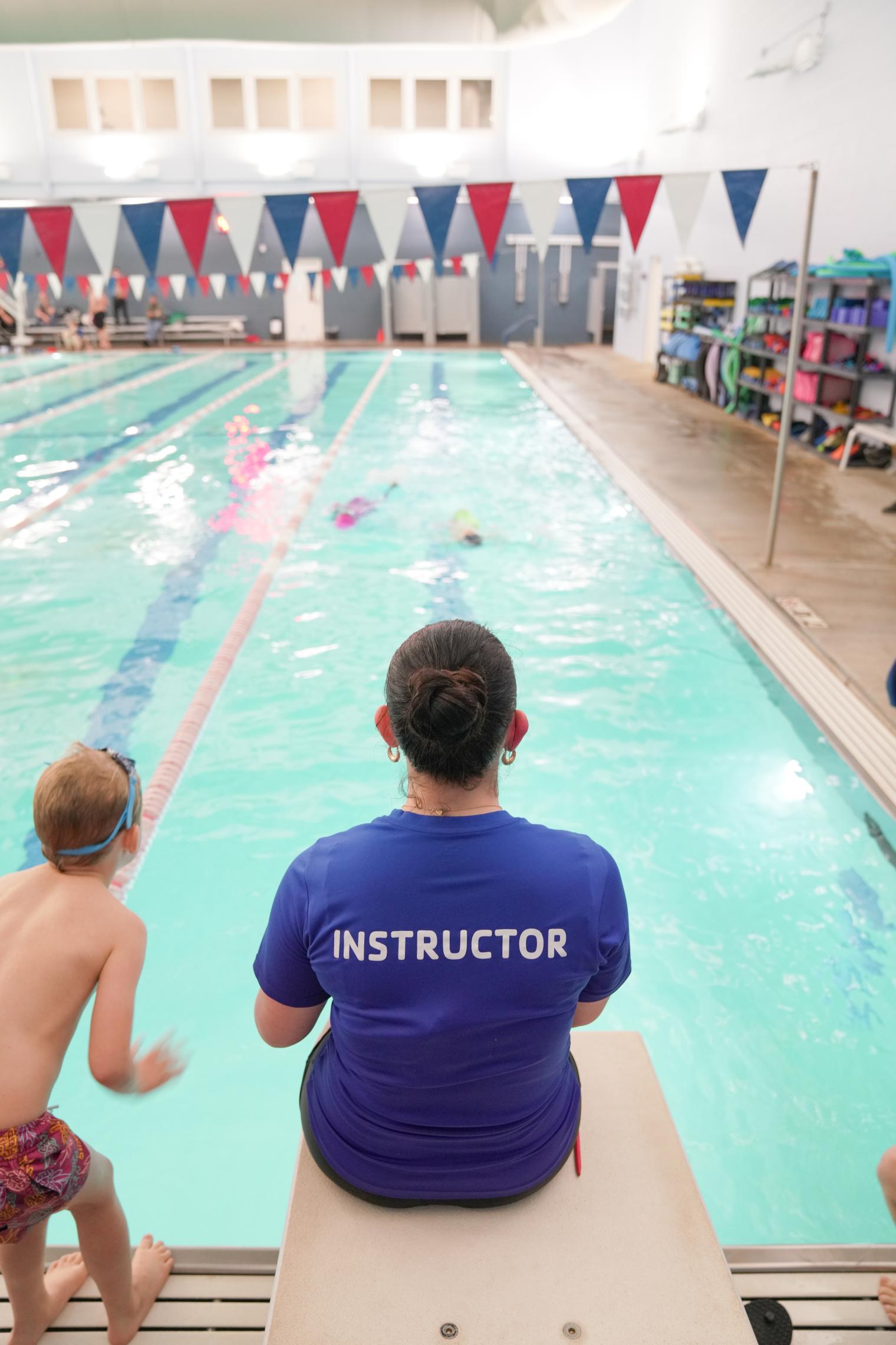 A swim instructor sits on the diving board
